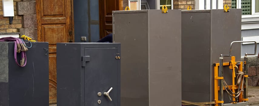 Several large safes are being moved outside a building, with workers organizing equipment in a bustling urban area.