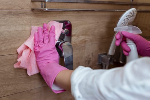 Close-up of female hands with rubber gloves washing the shower cabin and faucet in the bathroom. Housekeeping and maid.