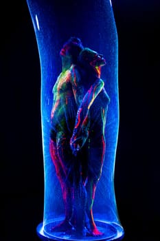Naked man and woman with colorful fluorescent body art standing in glow bubble tube