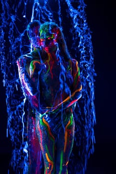 Nude man and woman with colorful body art embracing each other while standing under stream of water against black background