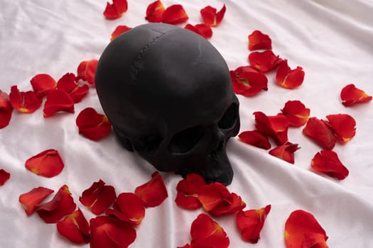 Black skull lying in red rose petals - love and death concept