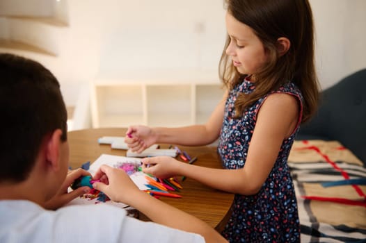 Two children playing with colorful pencils and craft materials at a table, focusing on creativity and collaboration in a warm, playful environment.