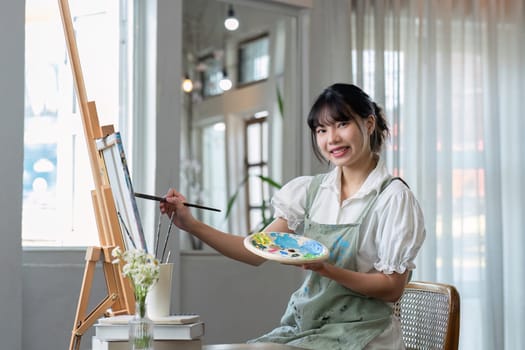 Young female artist works on abstract acrylic painting on canvas in art painting studio..