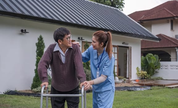 Asian woman caregiver helping senior man walking. Nurse assisting he old man patient at nursing home. Senior man using walker being helped by nurse at home. Elderly patient care and health lifestyle.