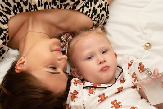 Family. Mom and little daughter are lying on the bed happy. Portrait of a woman and a beautiful little girl. View from above. Close-up.