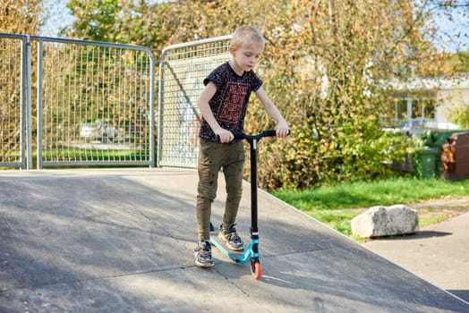 Child on kick scooter in park. Kids learn to skate roller board. Little boy skating on sunny summer day. Outdoor activity for children on safe residential street. Active sport for preschool kid. boy kid Roller park