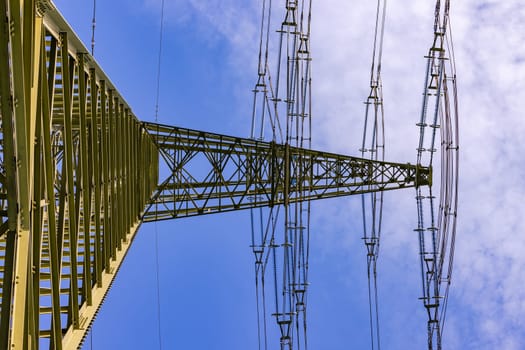 Massive and large high voltage pylon for electricity as power line for many overhead lines against blue sky with view upwards