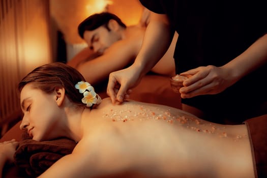 Couple customer having exfoliation treatment in luxury spa salon with warmth candle light ambient. Salt scrub beauty treatment in Health spa body scrub. Quiescent