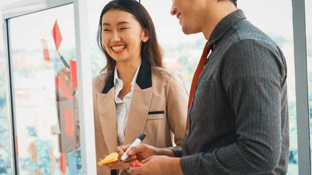 Business people work on project planning board in office and having conversation with coworker friend to analyze project development . They use sticky notes posted on glass to make it organized. Jivy