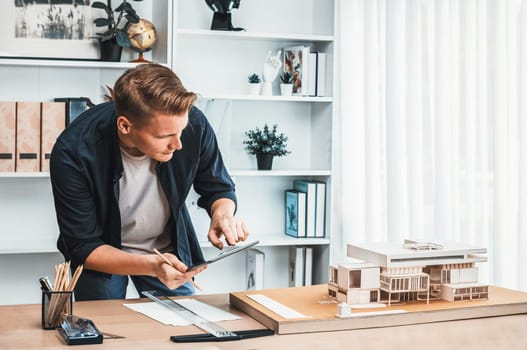 Architect designer studies elegant house model, reviewing structure design for improvement with construction plan on table. Creativity and innovation in architectural design. Iteration