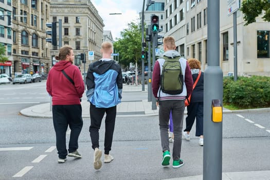 Group of people are crossing city road on green light of traffic light, street of big city background