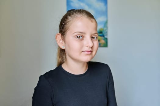 Headshot portrait of child girl 10 years old inside on background of light wall