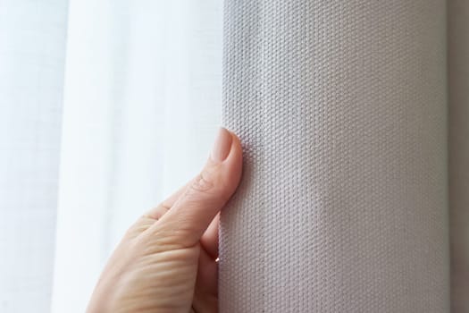 Close-up of a hand touching a gray curtain on a window