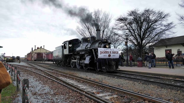 Strasburg, Pennsylvania, December 31, 2024 - A historic steam locomotive B9 is seen at a railway station as it prepares for its last journey, honoring James R. Rice. Train enthusiasts gather to witness this significant event on a cloudy day.