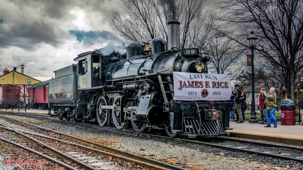 Strasburg, Pennsylvania, December 31, 2024 - A historic steam locomotive B9 is seen at a railway station as it prepares for its last journey, honoring James R. Rice. Train enthusiasts gather to witness this significant event on a cloudy day.