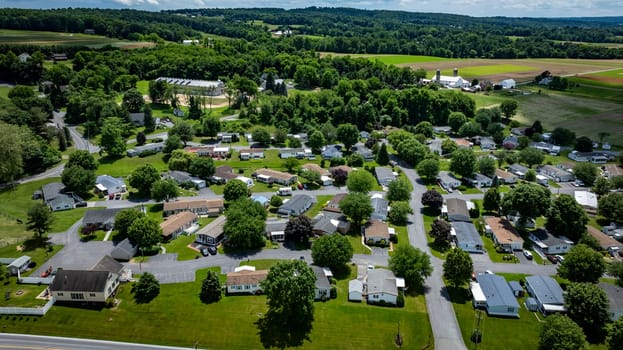 Aerial view of a tranquil rural community featuring various Mobile, Prefab, Manufactured houses situated near lush green fields and trees. The landscape shows harmonious blend of residences farmland.