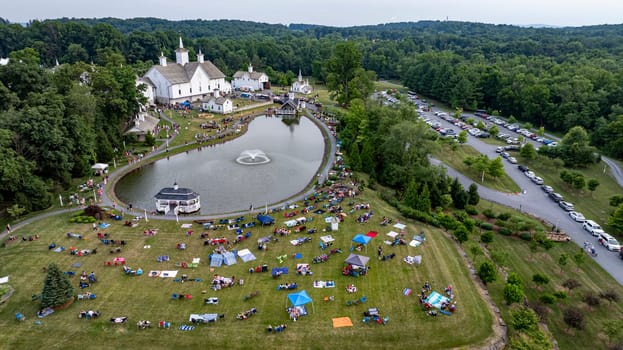 Elizabethtown, Pennsylvania, USA, July 4, 2024 - Charming Rural Fairground With A Scenic Pond, White Barns, Small Churches, And People Enjoying Picnics And Festivities On A Lush Green Lawn, Surrounded By Trees And Rolling Hills.