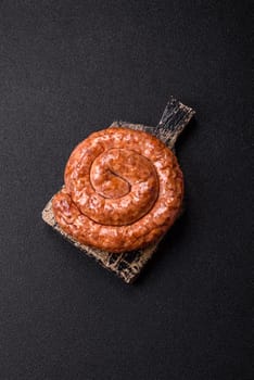 Delicious homemade sausage in the shape of a snail or spiral, with salt and spices on a dark concrete background
