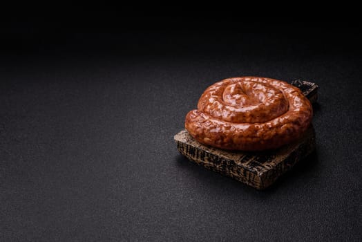 Delicious homemade sausage in the shape of a snail or spiral, with salt and spices on a dark concrete background