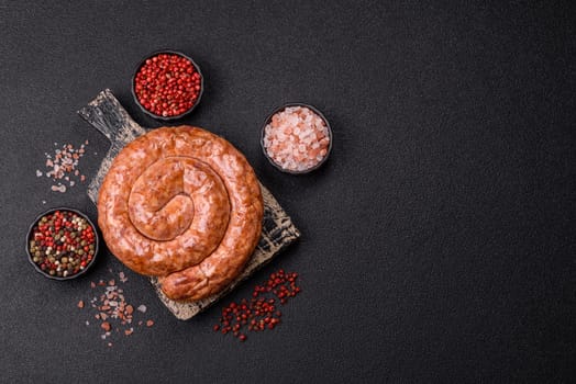 Delicious homemade sausage in the shape of a snail or spiral, with salt and spices on a dark concrete background