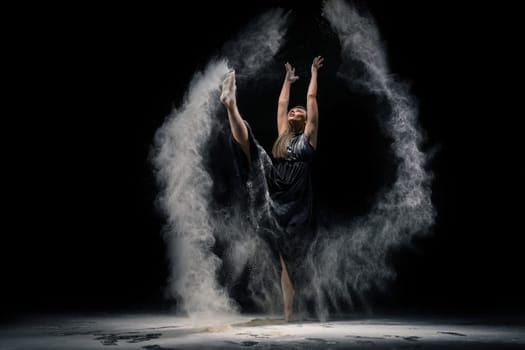 Full length slim female in bra and panties throwing sand in air and dancing against black background