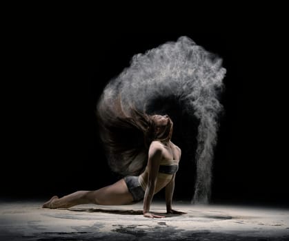 Full body side view of fit young female in sportive outfit performing yoga pose with cloud of dust from hair
