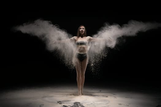 seductive brunette female in sport wear throwing dust with outstretched arms against black background
