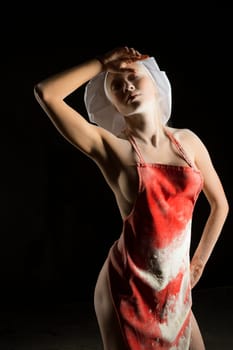 Full body sexy woman in dirty apron and chef cap wiping forehead with closed eyes while standing on dust against black background