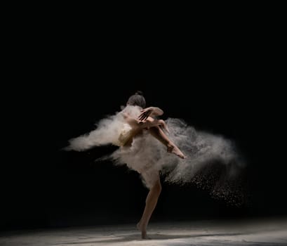 Full length slim female in body cloth dancing against black background in cloud of dust