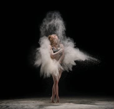Full length barefoot female dancer embracing boy while standing in cloud of dust against black background