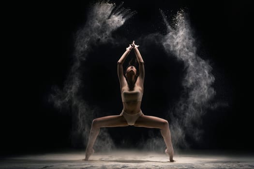 Full length slim female in bra and panties throwing sand in air and dancing against black background