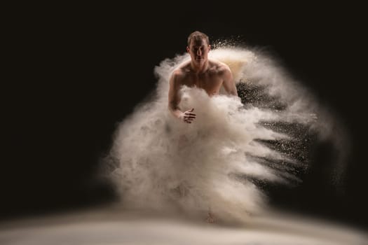 Full body of muscular guy looking at camera and dancing in cloud of dust against black background