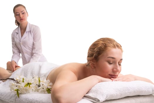 Professional female masseur massaging foots of relaxed woman lying on table on white background