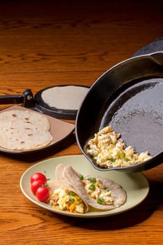 Scrambled eggs in a skillet pouring into a hand made flour tortilla.