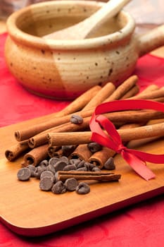Chocolate chips and a pile of cinnamon stick together on a cutting board.