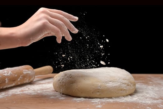 A close up of a hand sprinking flour on a piece of dough on a board.
