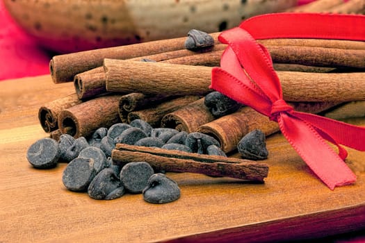 Chocolate chips and a pile of cinnamon stick together on a cutting board.
