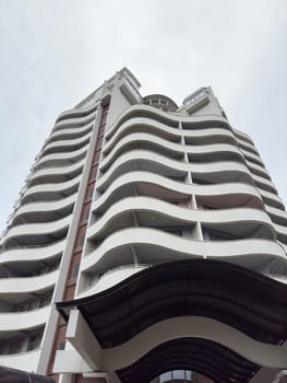 A contemporary building with flowing curved balconies rises against a cloudy sky. The structure's unique design showcases modern architecture in an urban setting.