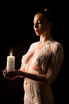 Topless female model with wax on shoulders Look at carrying burning candle on black background