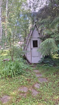 Cozy wooden bio toilet with A-shaped frame in a lush forest landscape.
