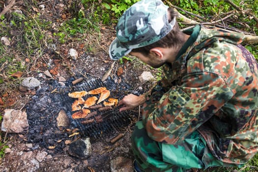 Soldier is grilling meat on a makeshift barbecue during a forest survival training exercise