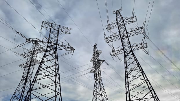 Several high voltage power lines standing tall against a cloudy sky. Industrial scene illustrating energy distribution and infrastructure