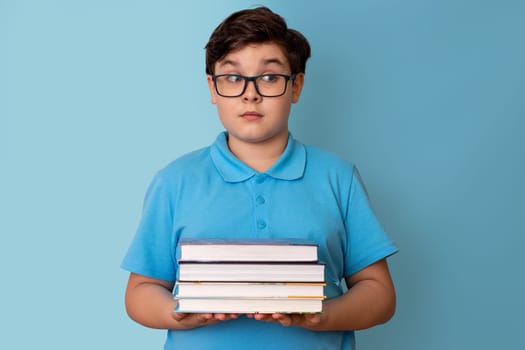 A surprised teenage boy with glasses hold a stack of books, looking away.Copy space