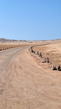 A road in a desert area fenced with homemade pyramids made of stones.Vertical