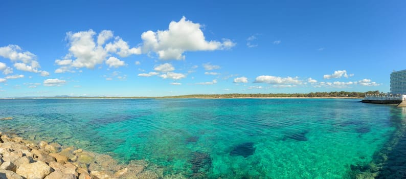 Panoramic view of Mallorca, Balearic Islands, featuring crystal-clear turquoise water, rocky shoreline, and a blue sky with scattered clouds.
