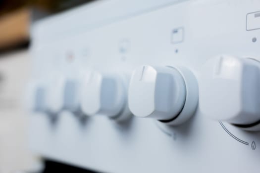 Close-up in focus: one rotary control knob at the kitchen white gas stove on the other knobs out of focus. Concept of cooking, temperature control, cooking modes. High quality photo