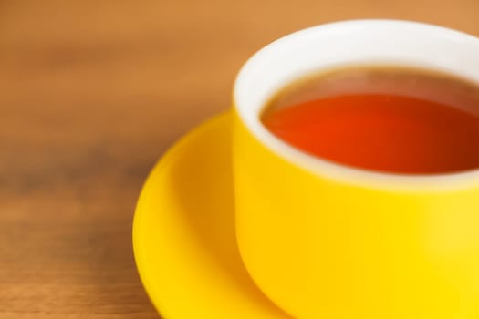 A bright yellow cup with a saucer to which fragrant tea is poured stands on the left, part of the mug is visible on a wooden background. High quality photo