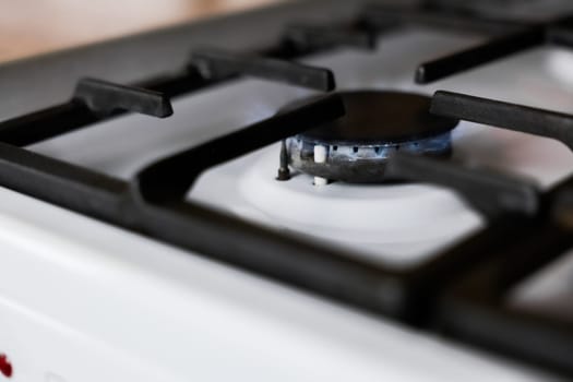 Close-up of a white gas stove with a black cast-iron grate and a black burner on which a blue fire burns. Gas stove, cooking concept. High quality photo