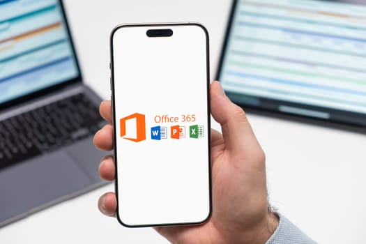 PRAGUE, CZECHIA - JULY, 2025: Microsoft Office 365 logo on the screen of smartphone in mans hand and laptop on the background