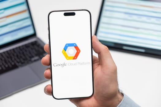 PRAGUE, CZECHIA - JULY, 2024: Google Cloud Platform logo on the screen of smartphone in mans hand and laptop on the background